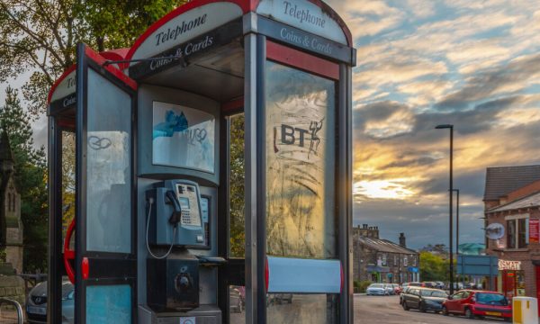 A phone-box with light graffiti in front of a sunset.
