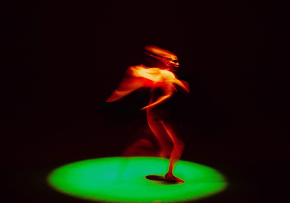 An illuminated orange figure runs on a green spotlit circle