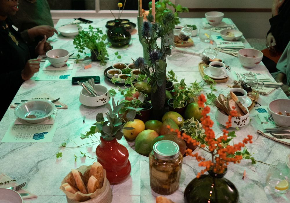 A table of food, plates and people around the edge, with green lighting