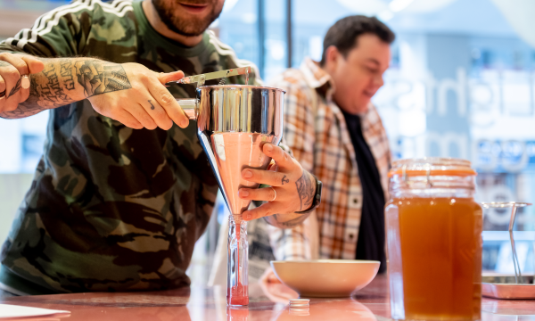 A person pours bright pink sauce through a silver funnel into a glass bottle