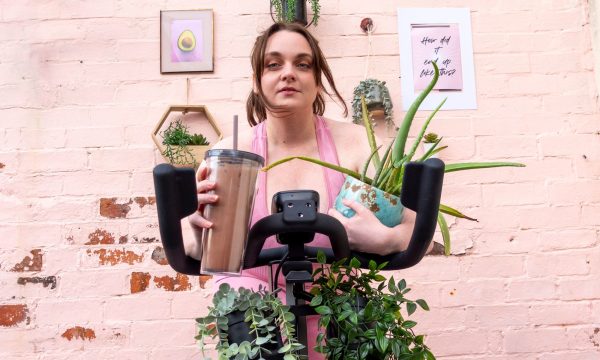 Lydia in milennial pink on a spin bike clutches a smoothie and a pot plant