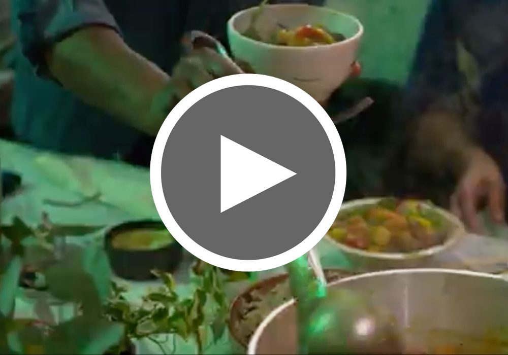 A play button over a slightly blurry image of people around a table, green lit