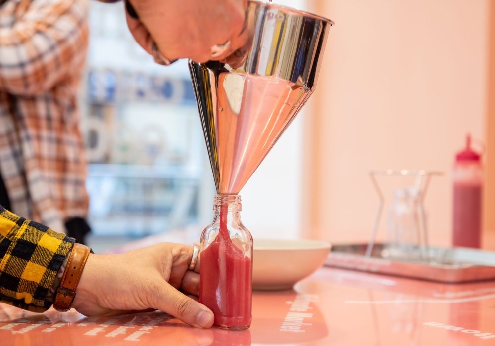 A photo of a silver funnel with pink sauce being bottled