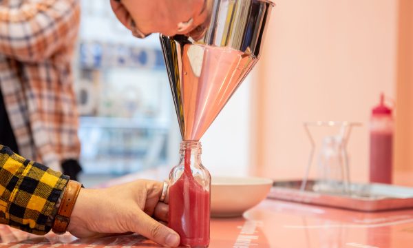 A photo of a silver funnel with pink sauce being bottled