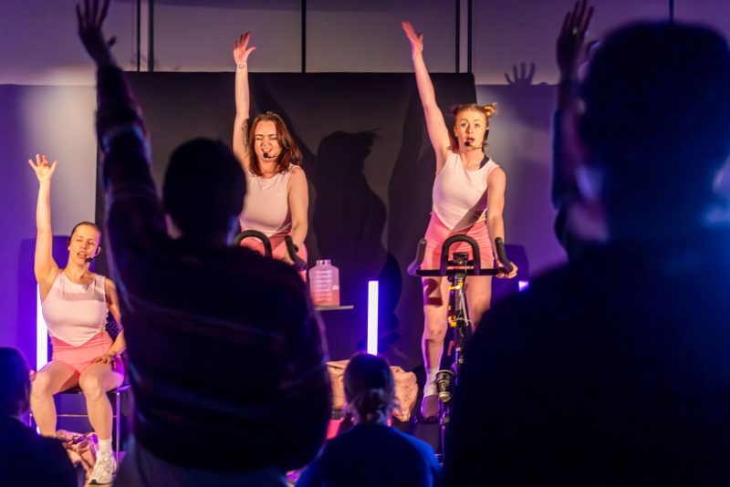 Three instructors wearing pink lead a spin class 