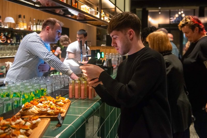 A person photographs food and Leeds Sauce bottles